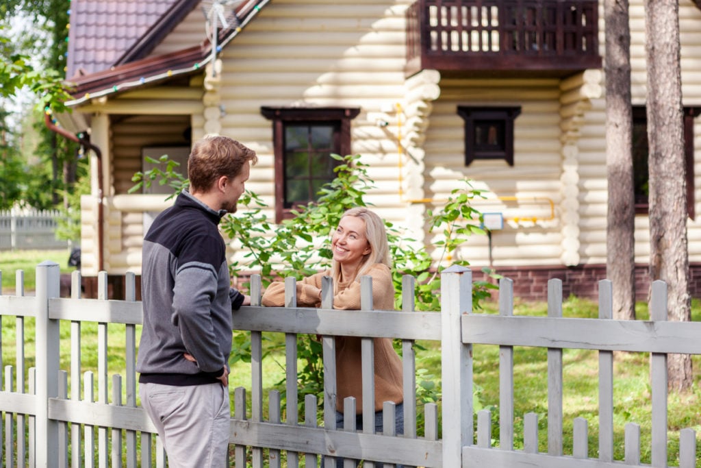 Middle aged man meeting smiling female neighbor in countryside and talking cheerfully to her over fence